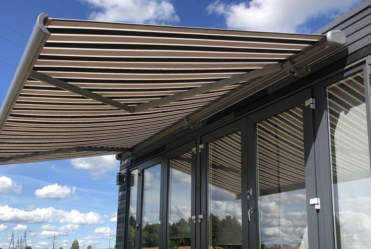 Utfällbar markis med randigt tygöverdrag monterad över terrassglasning