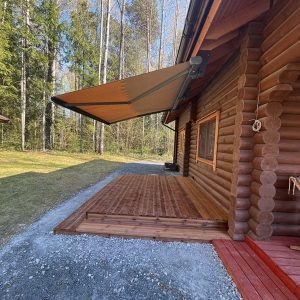 Brun markis utfälld över trädäck vid träkoja med granar i bakgrund
