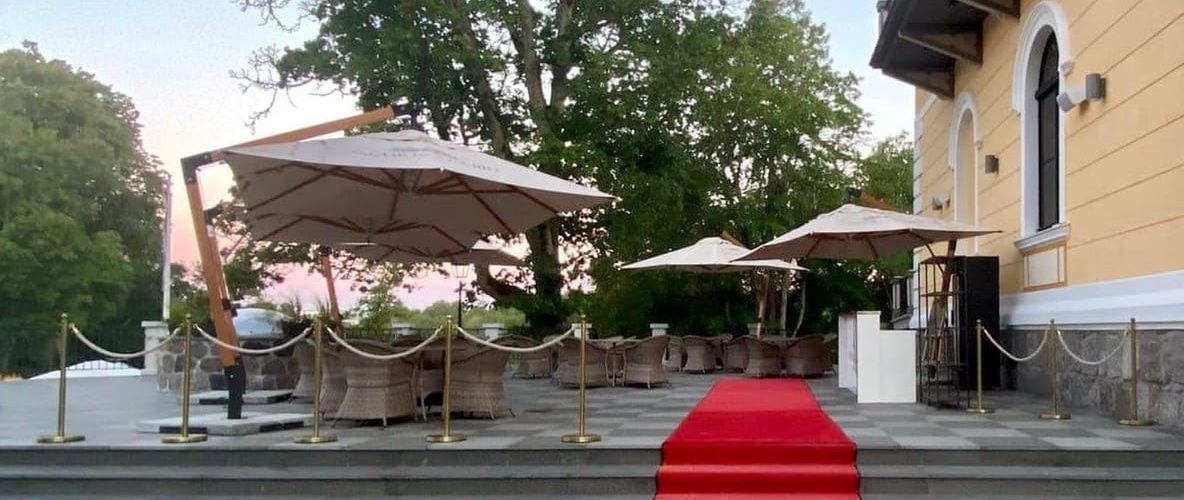 Beige väriset kantoparasollt ylellisellä på terrass punaisella matolle johtavalla portaalla