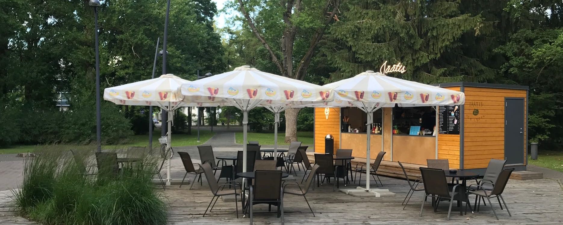 vit ulkotältduk parasoll punaisen ja keltaisen kuvioinnilla puistossa orangesen kahvion