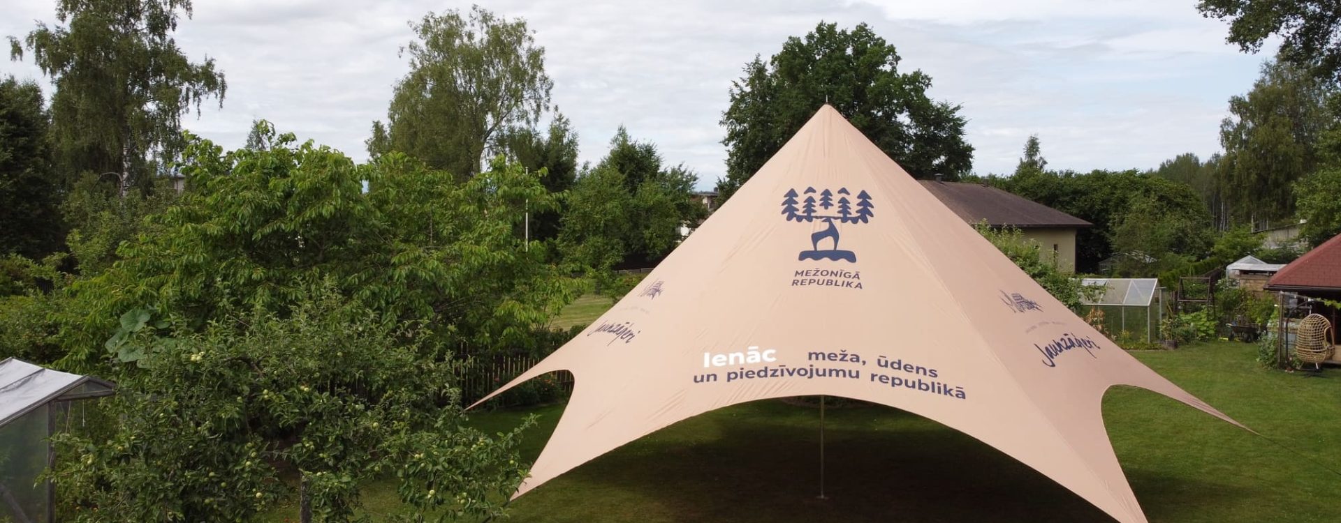 Star tält — beige stjärnformad tält på gräsmatta omgiven av grönska